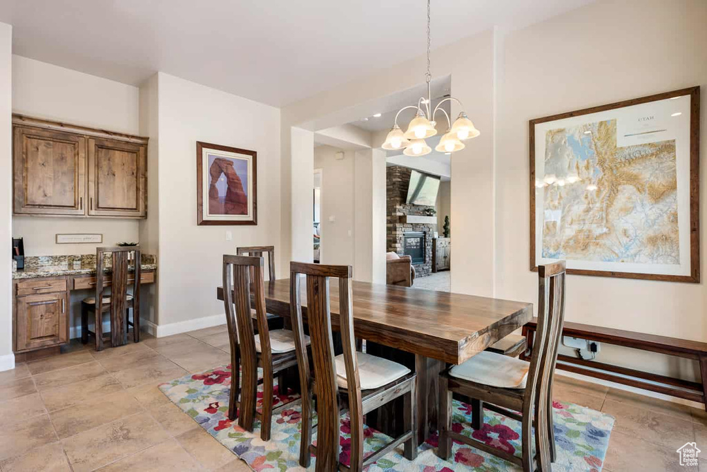 Dining area featuring baseboards, a notable chandelier, a stone fireplace, and light tile patterned floors