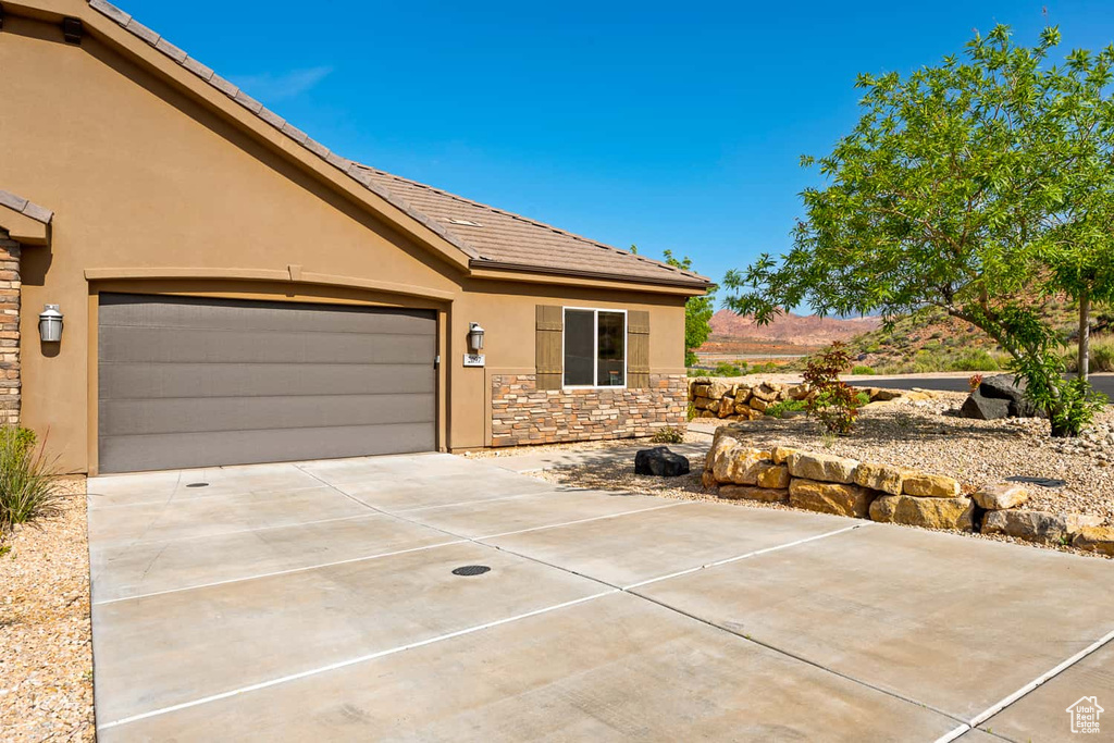 Ranch-style home with an attached garage, stucco siding, stone siding, and concrete driveway