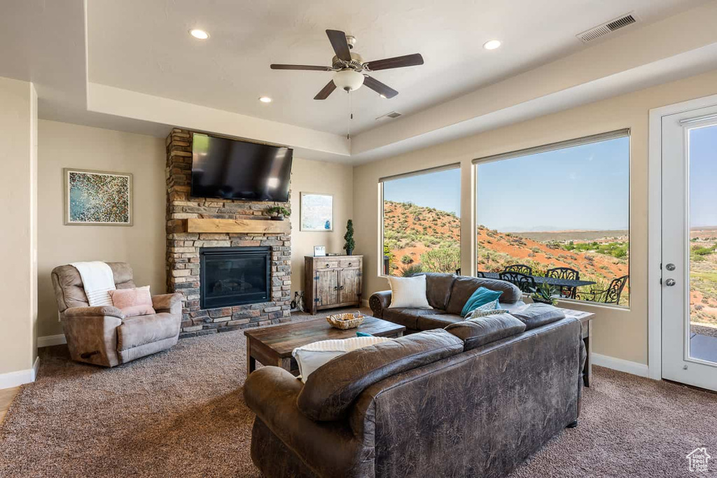 Living room with a ceiling fan, visible vents, a fireplace, baseboards, and carpet