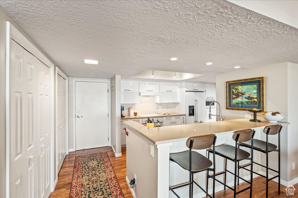 Kitchen featuring a peninsula, light wood-style floors, a kitchen breakfast bar, high quality fridge, and white cabinets