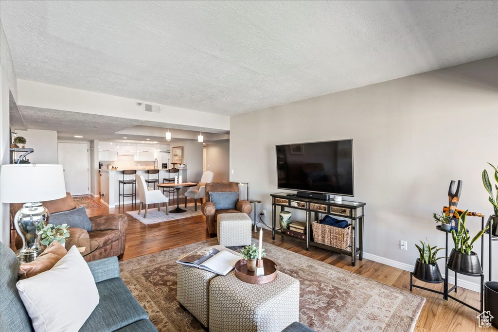 Living room featuring wood finished floors, baseboards, a textured ceiling, and visible vents