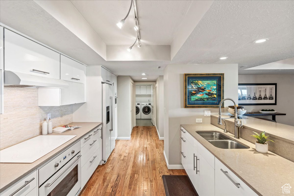 Kitchen featuring independent washer and dryer, a sink, white cabinetry, cooktop, and under cabinet range hood