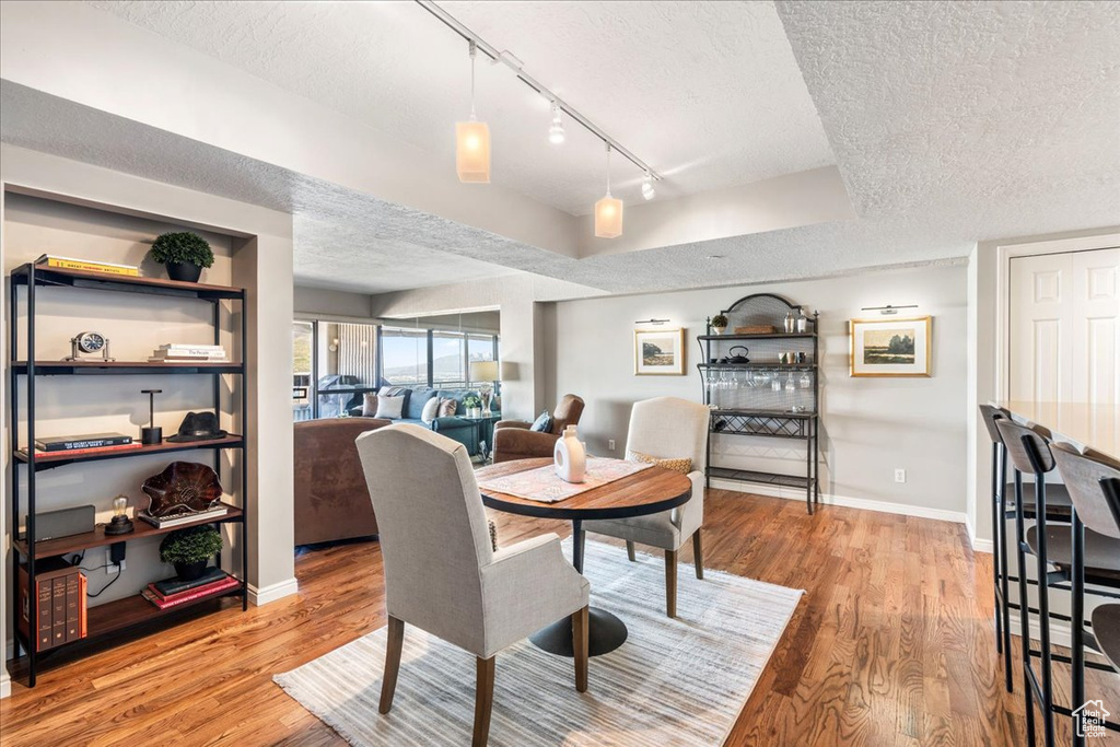 Dining room featuring baseboards, rail lighting, a textured ceiling, and wood finished floors
