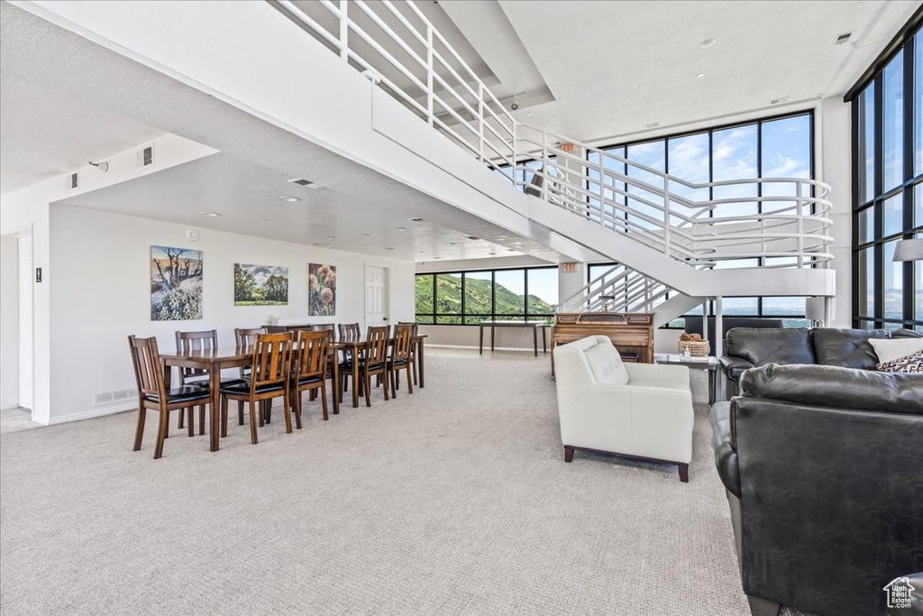 Carpeted living area with stairs, baseboards, visible vents, and a high ceiling