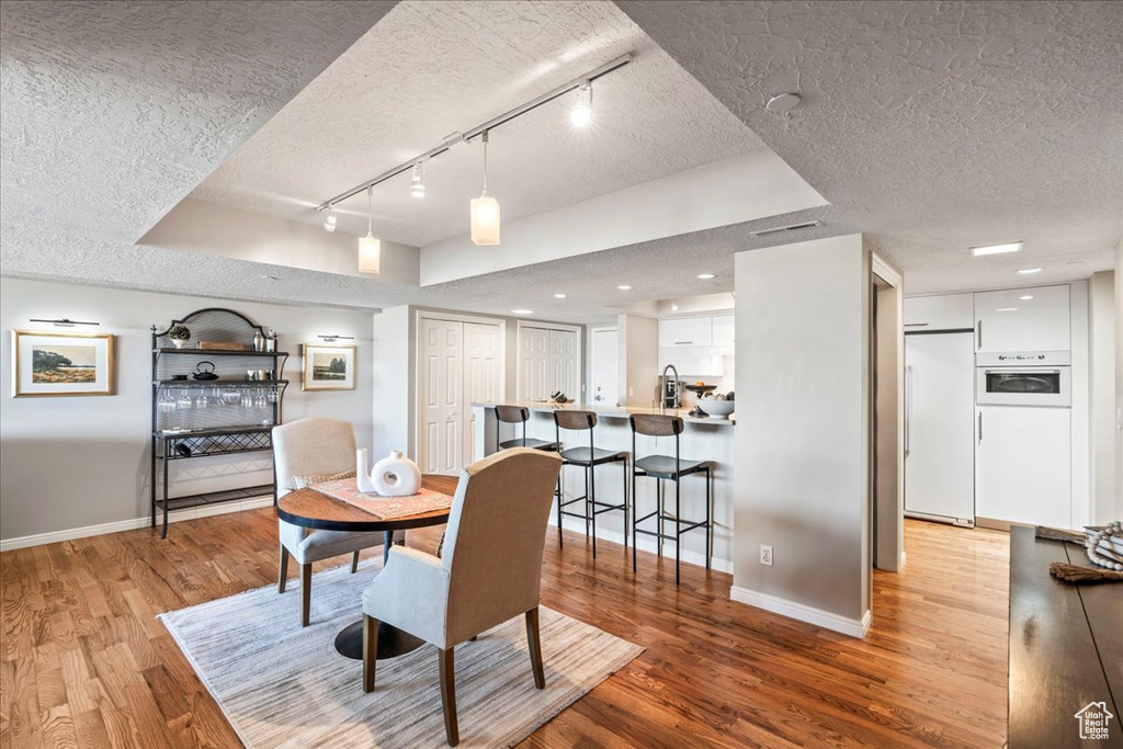 Dining room featuring a textured ceiling, track lighting, baseboards, and wood finished floors
