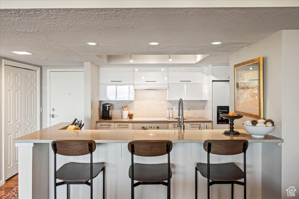 Kitchen featuring a textured ceiling, white cabinets, and a kitchen bar