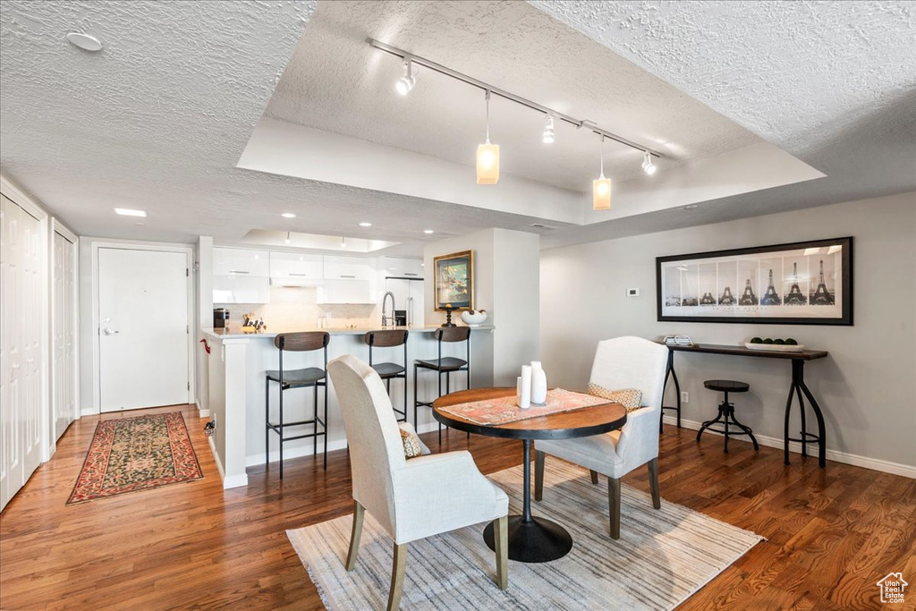 Dining space featuring baseboards, a raised ceiling, a textured ceiling, and wood finished floors