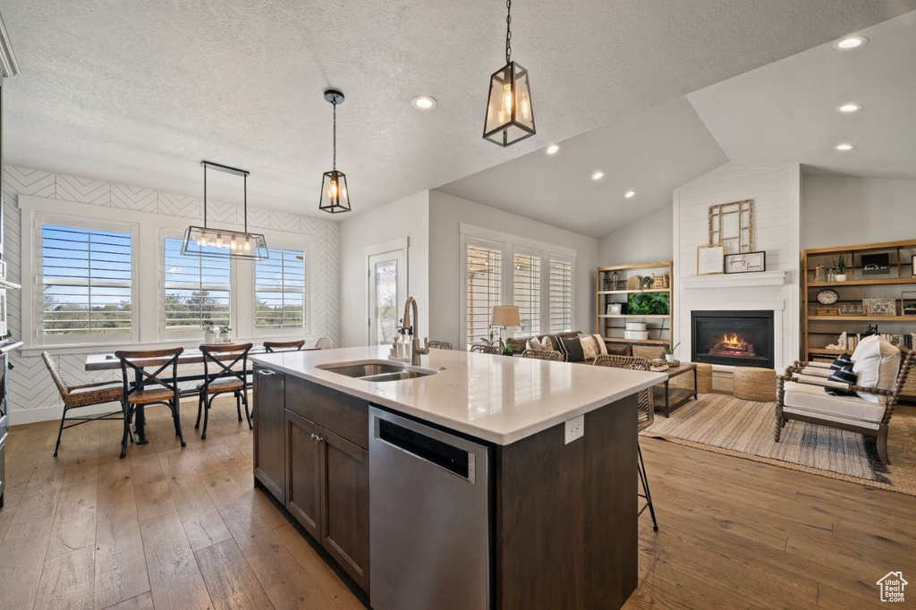 Kitchen with stainless steel dishwasher, a sink, dark brown cabinetry, and hardwood / wood-style flooring