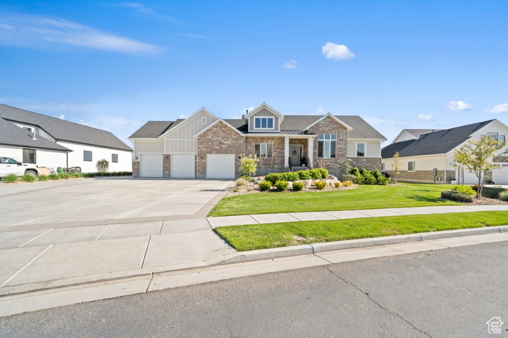 View of front of home featuring board and batten siding, a front yard, a garage, concrete driveway, and stone siding