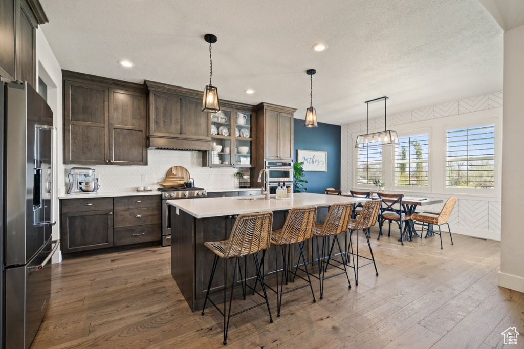 Kitchen featuring dark brown cabinetry, a breakfast bar area, light countertops, light wood finished floors, and stainless steel appliances