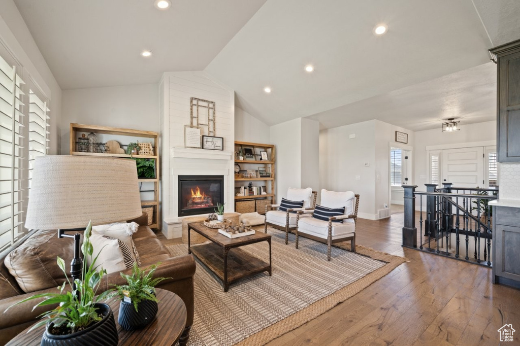Living area with lofted ceiling, wood finished floors, baseboards, recessed lighting, and a large fireplace