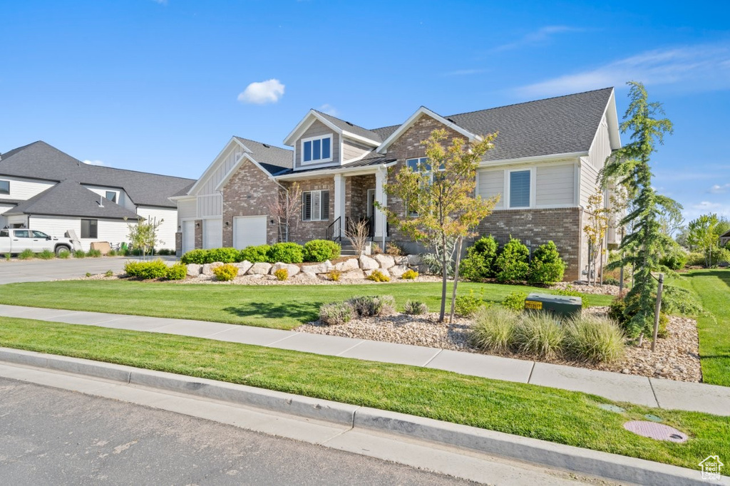 Craftsman house featuring an attached garage, stone siding, brick siding, a front yard, and concrete driveway