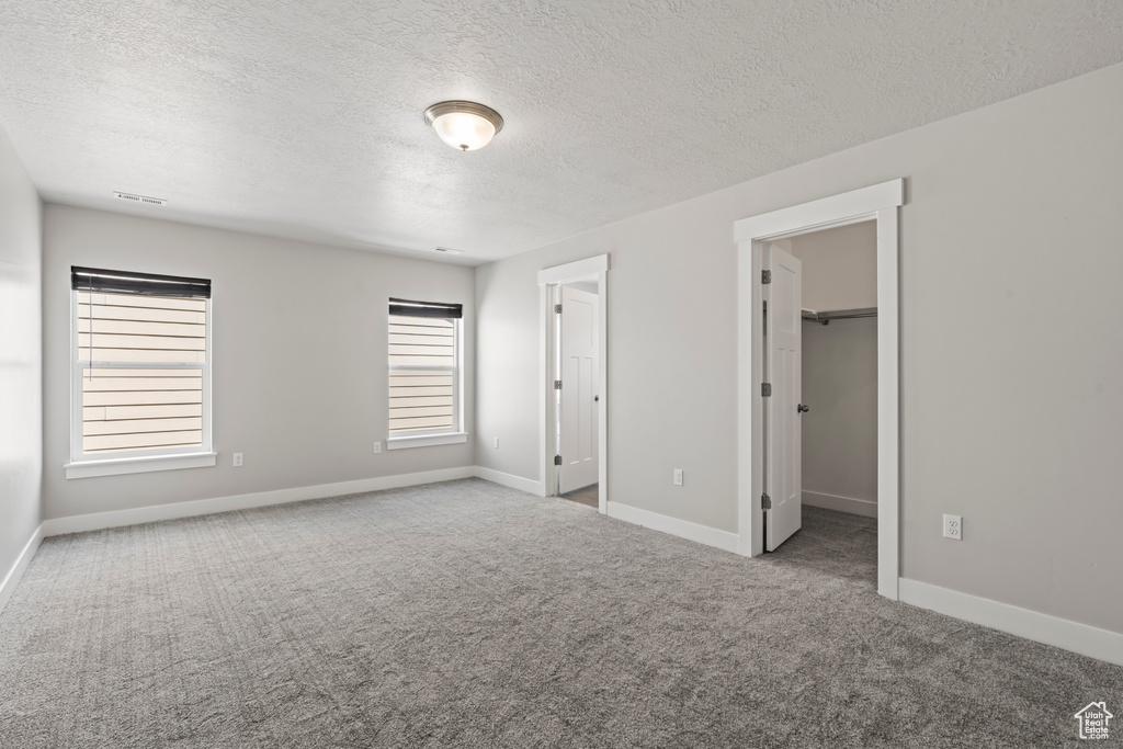 Unfurnished bedroom with a textured ceiling, visible vents, baseboards, a spacious closet, and carpet