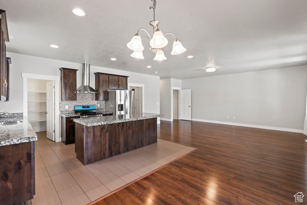 Kitchen with dark brown cabinetry, a kitchen island, wall chimney exhaust hood, a sink, and appliances with stainless steel finishes