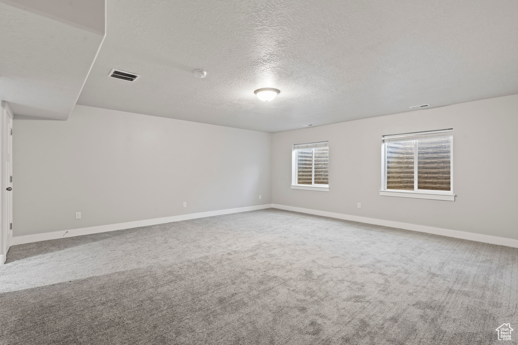 Carpeted spare room featuring visible vents, a textured ceiling, and baseboards