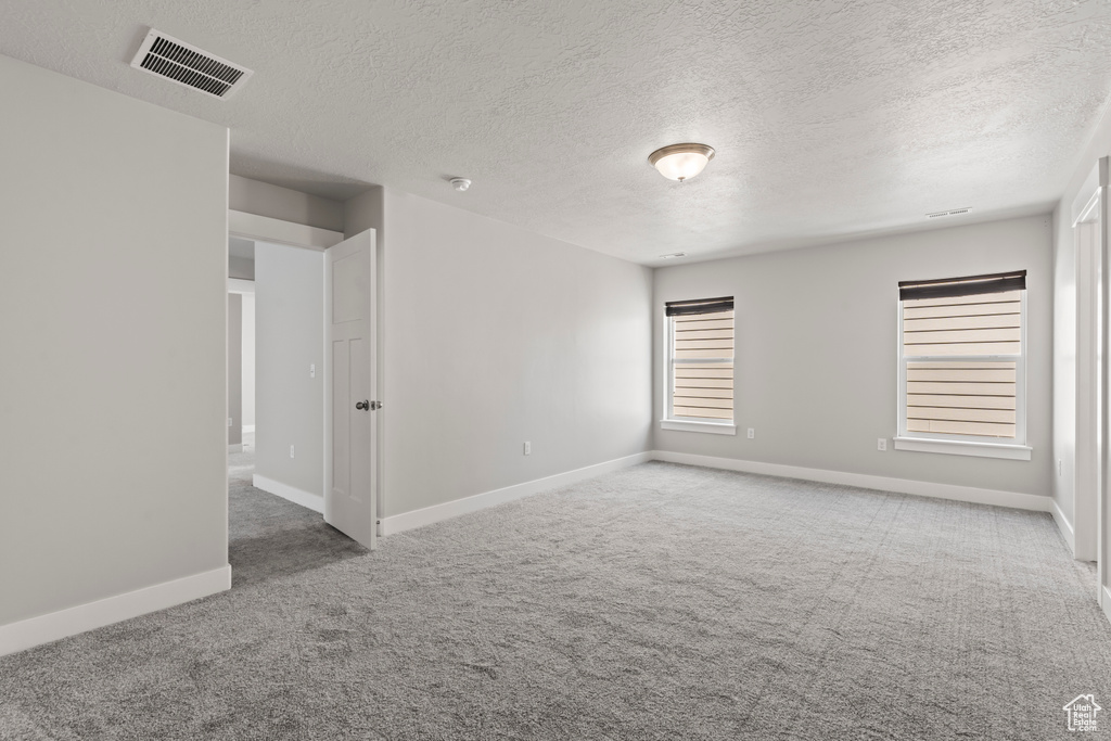 Empty room featuring visible vents, carpet flooring, baseboards, and a textured ceiling