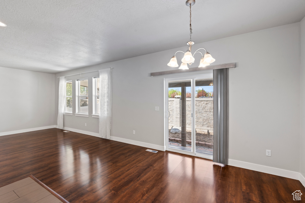 Unfurnished room featuring baseboards, a textured ceiling, wood finished floors, and a chandelier