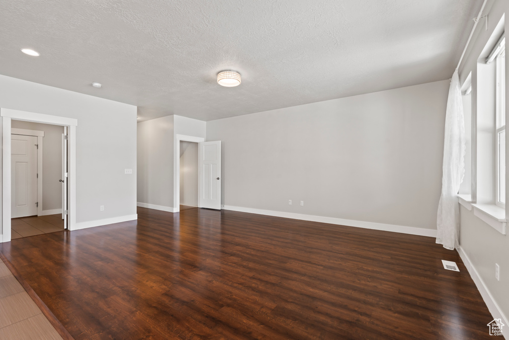 Unfurnished room featuring visible vents, a textured ceiling, dark wood-type flooring, and baseboards