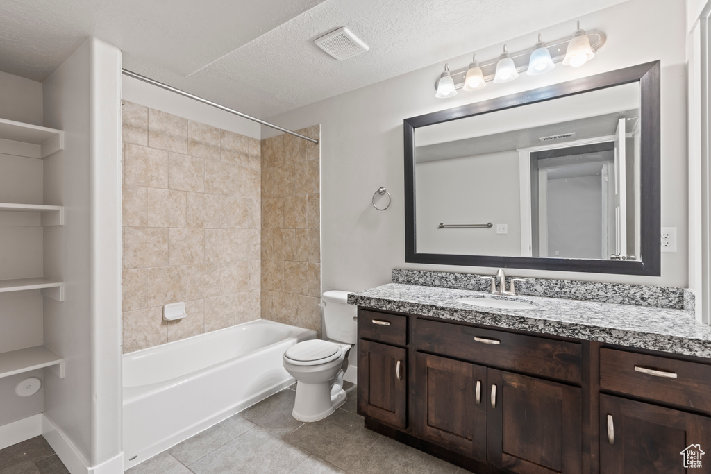 Bathroom with a textured ceiling, tile patterned floors, vanity, toilet, and washtub / shower combination