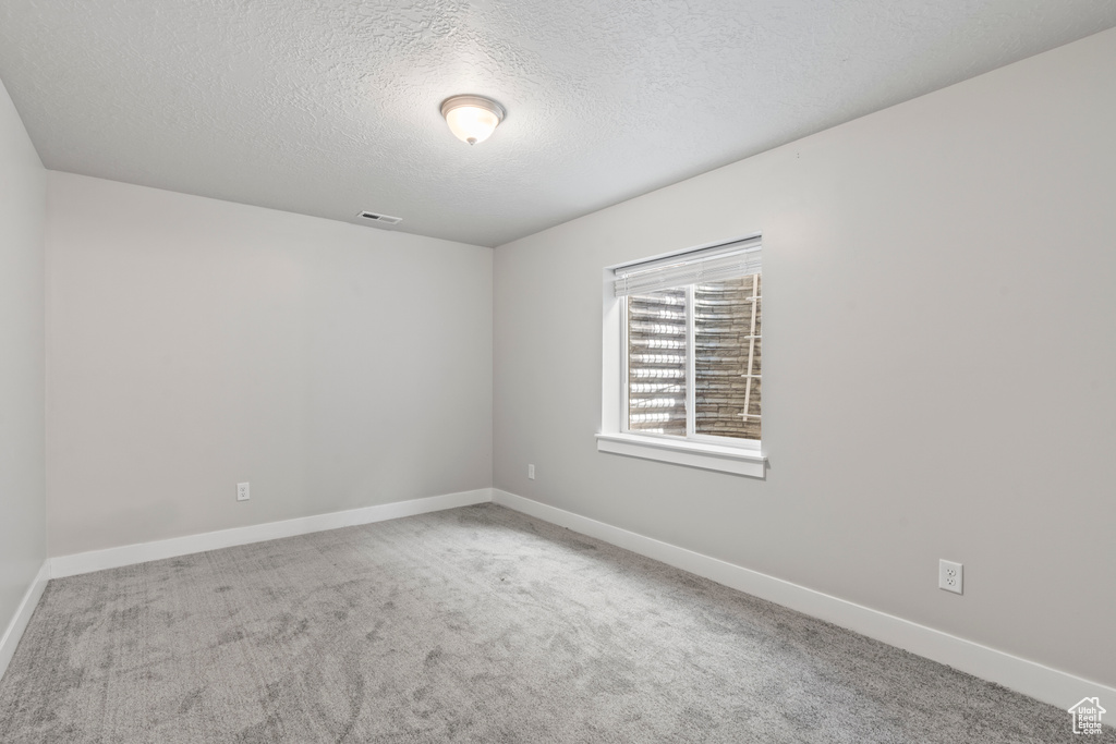 Carpeted empty room with baseboards, a textured ceiling, and visible vents