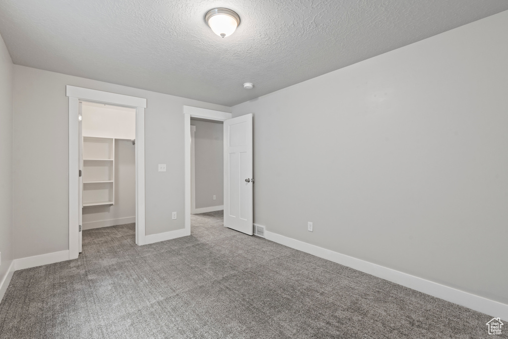Unfurnished bedroom with a closet, baseboards, a walk in closet, a textured ceiling, and carpet