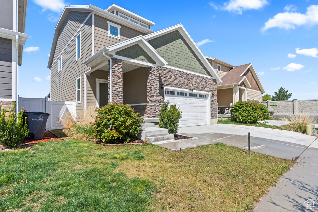 View of front facade featuring a front yard, fence, concrete driveway, an attached garage, and stone siding