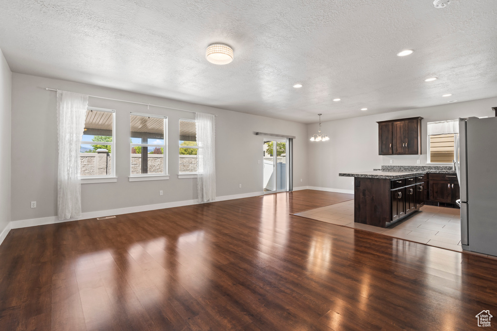 Unfurnished living room featuring an inviting chandelier, a textured ceiling, recessed lighting, baseboards, and wood finished floors