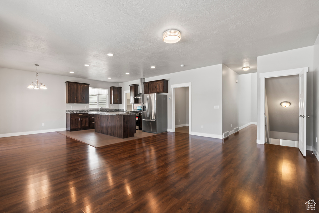 Unfurnished living room featuring an inviting chandelier, dark wood-style flooring, baseboards, a textured ceiling, and a sink