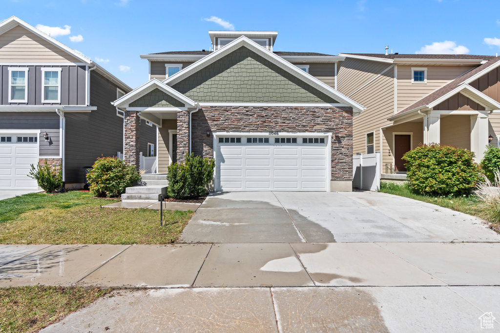 Craftsman-style home featuring an attached garage, a front lawn, stone siding, and concrete driveway