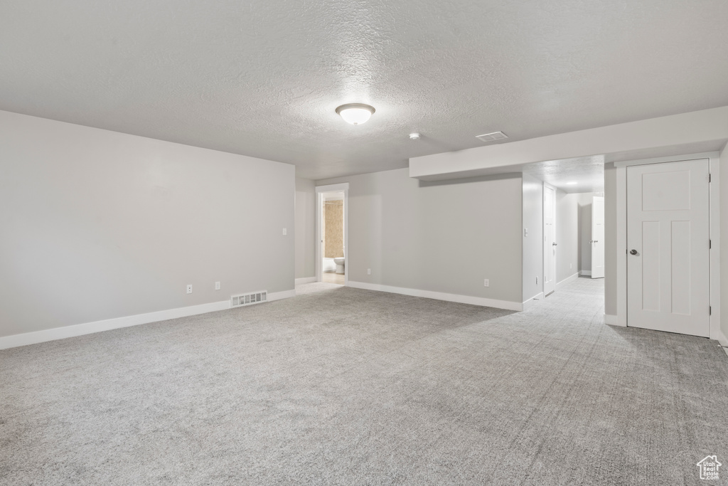 Carpeted empty room featuring baseboards, a textured ceiling, and visible vents