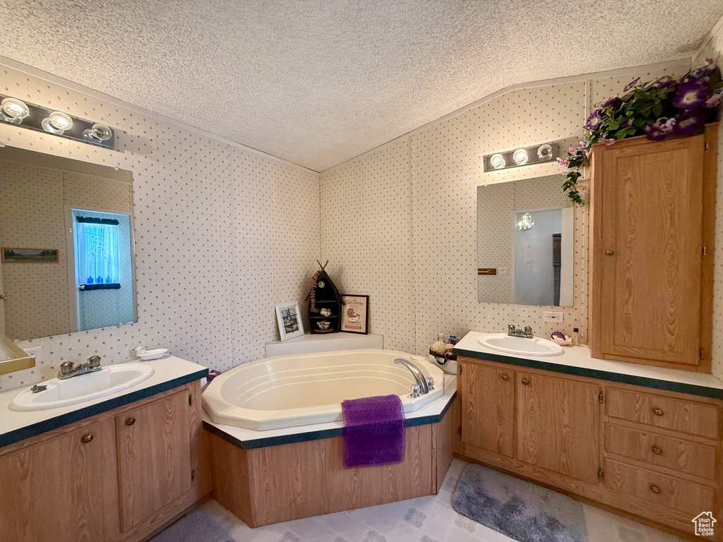 Bathroom featuring a sink, a bath, vaulted ceiling, and a textured ceiling