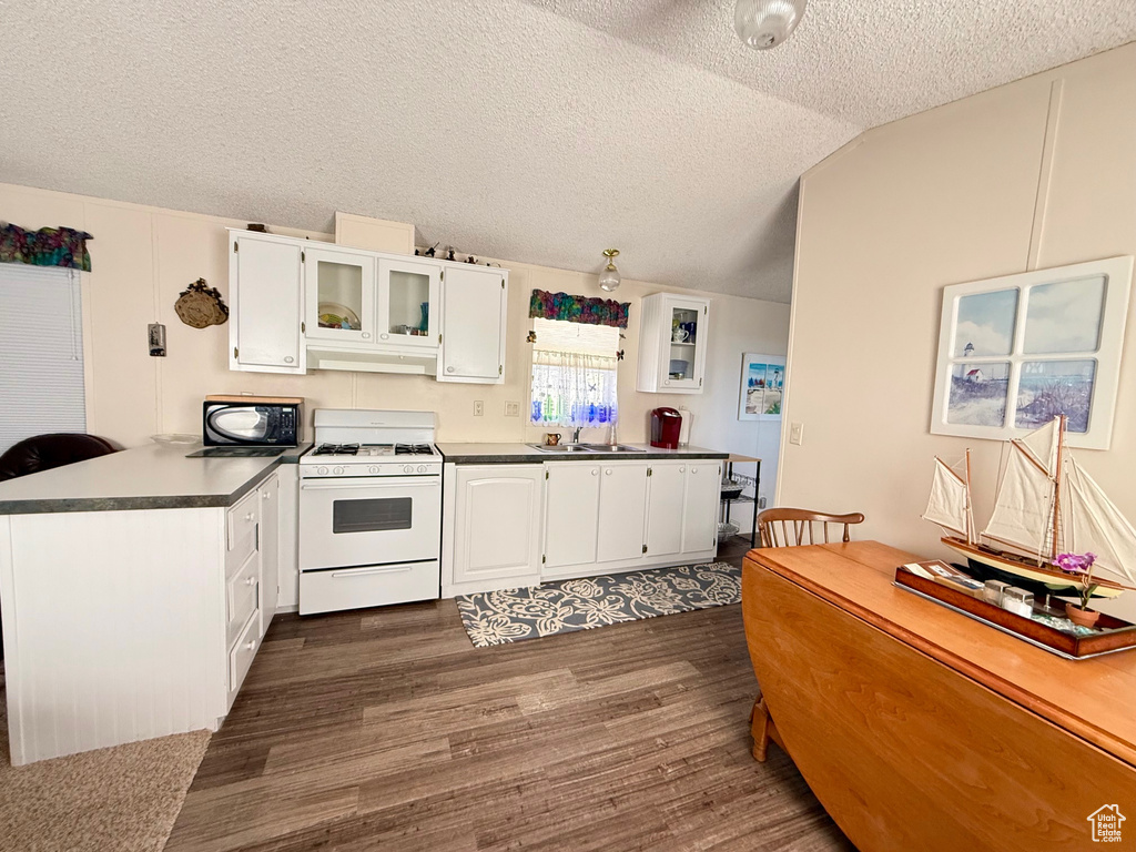 Kitchen with white gas range oven, black microwave, a peninsula, white cabinetry, and dark wood-type flooring