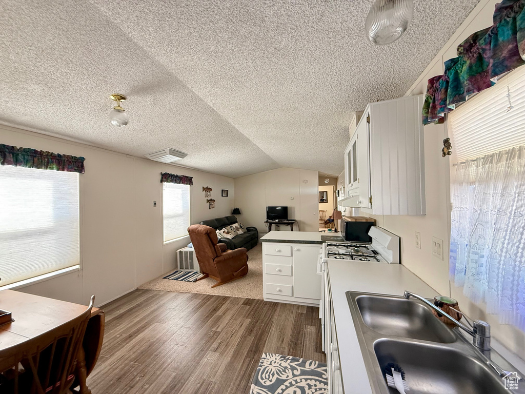 Kitchen with white gas range oven, a sink, a textured ceiling, under cabinet range hood, and dark wood-style floors