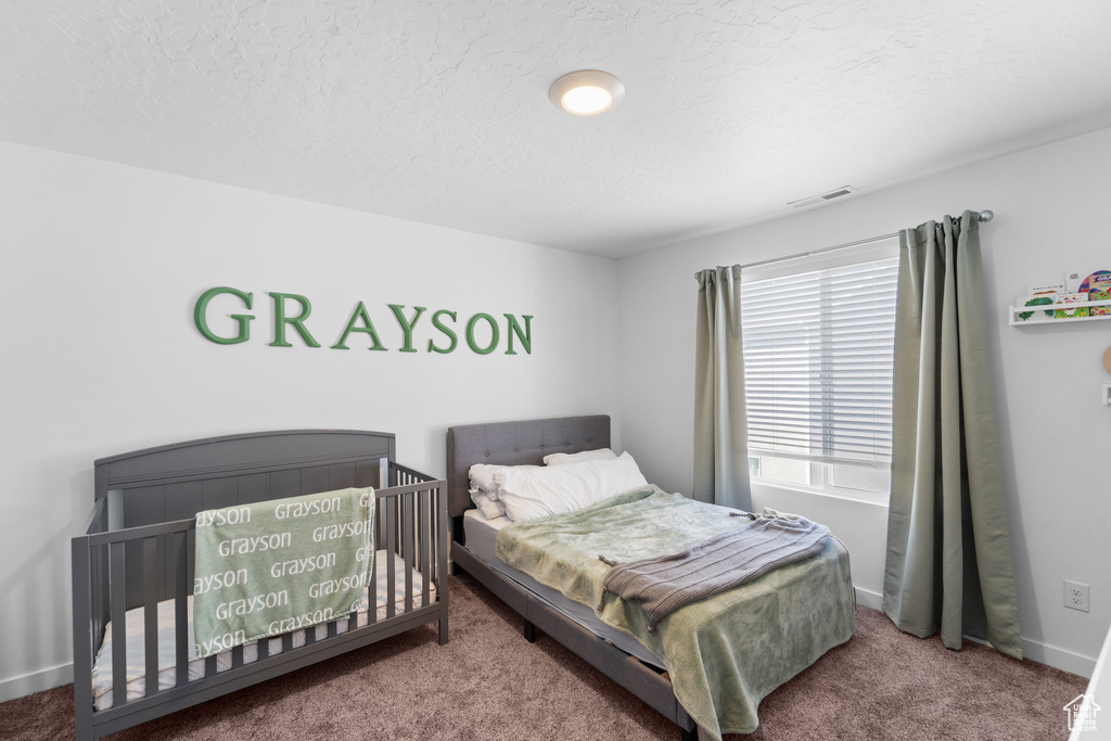 Carpeted bedroom with visible vents, a textured ceiling, baseboards, and multiple windows