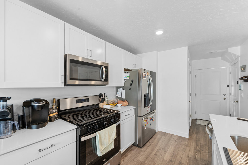 Kitchen with light countertops, appliances with stainless steel finishes, white cabinets, and light wood-style flooring
