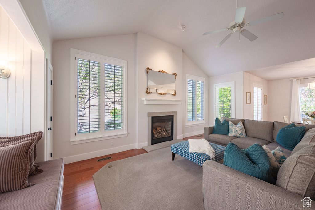Living room featuring visible vents, lofted ceiling, wood finished floors, baseboards, and a fireplace with raised hearth