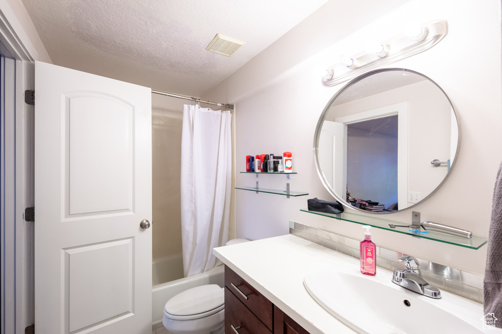 Full bath with vanity, toilet, a textured ceiling, shower / bath combination with curtain, and visible vents