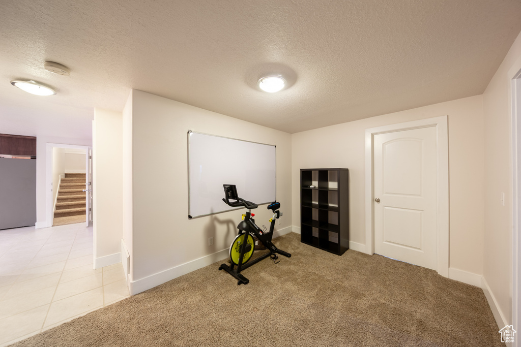 Workout room with a textured ceiling, light colored carpet, and baseboards