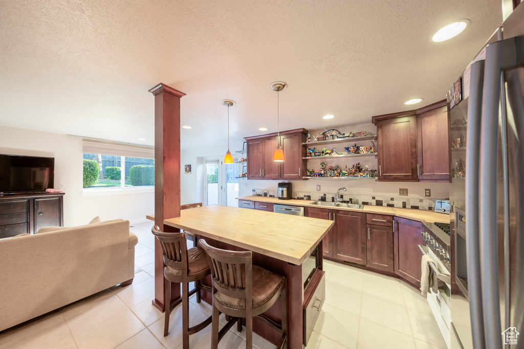 Kitchen featuring open shelves, a sink, a textured ceiling, butcher block countertops, and stainless steel appliances