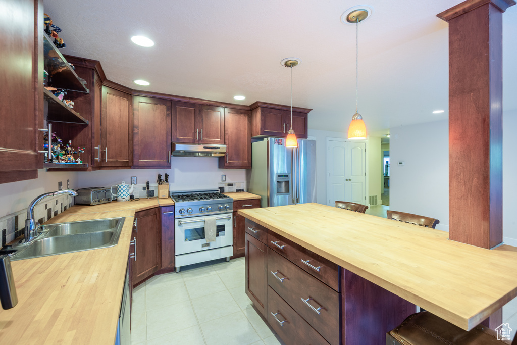 Kitchen with butcher block counters, gas range, stainless steel fridge, under cabinet range hood, and a sink