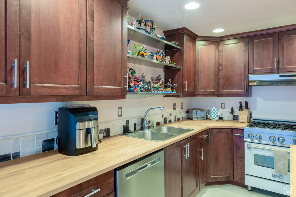 Kitchen with butcher block countertops, recessed lighting, under cabinet range hood, a sink, and appliances with stainless steel finishes