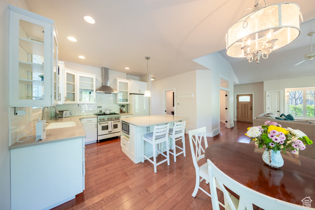 Kitchen with range with two ovens, wall chimney exhaust hood, a sink, stainless steel microwave, and light wood-style flooring