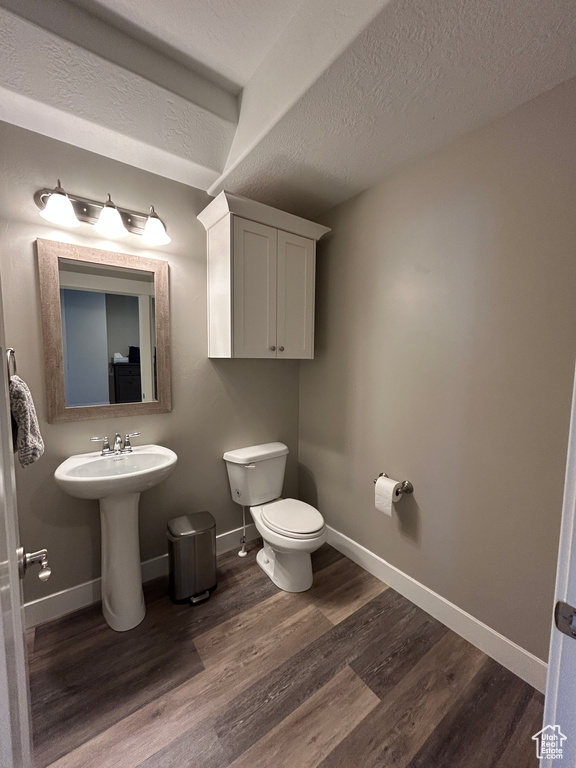 Bathroom with baseboards, a textured ceiling, wood finished floors, and toilet