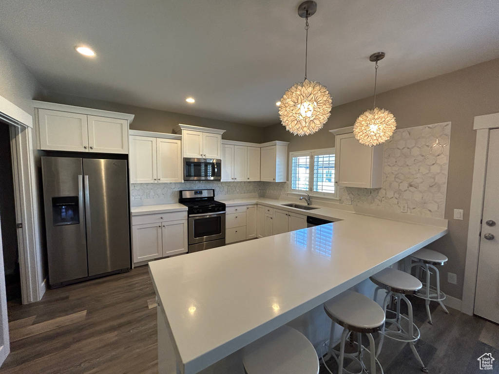 Kitchen with backsplash, dark wood-style flooring, a sink, a peninsula, and stainless steel appliances