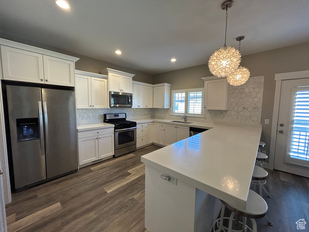 Kitchen featuring decorative backsplash, a peninsula, a kitchen bar, a sink, and appliances with stainless steel finishes