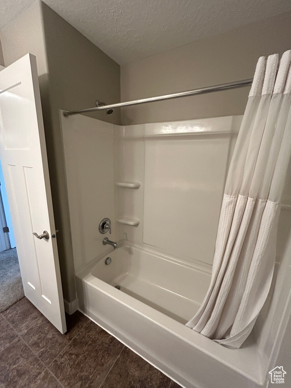 Bathroom with tile patterned floors, shower / bathtub combination with curtain, and a textured ceiling