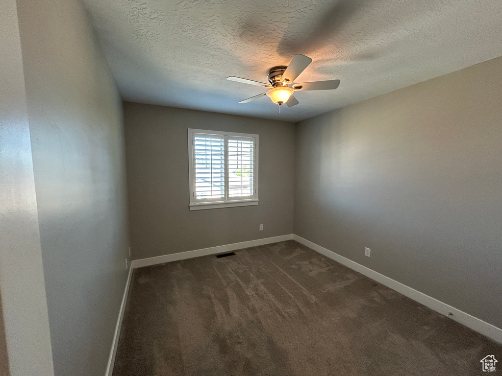Empty room with ceiling fan, a textured ceiling, visible vents, baseboards, and dark carpet