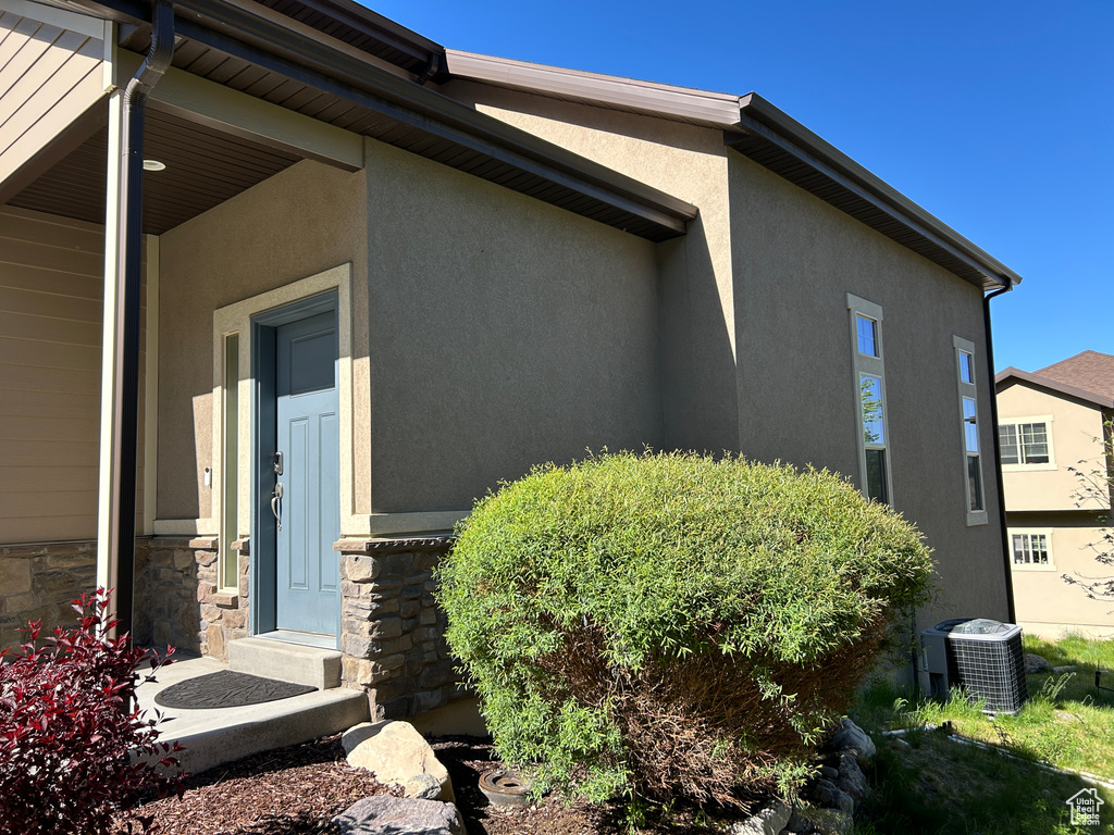 View of side of property featuring stucco siding, cooling unit, and stone siding