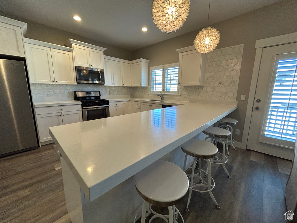 Kitchen featuring decorative backsplash, dark wood-style flooring, a kitchen breakfast bar, a sink, and stainless steel appliances