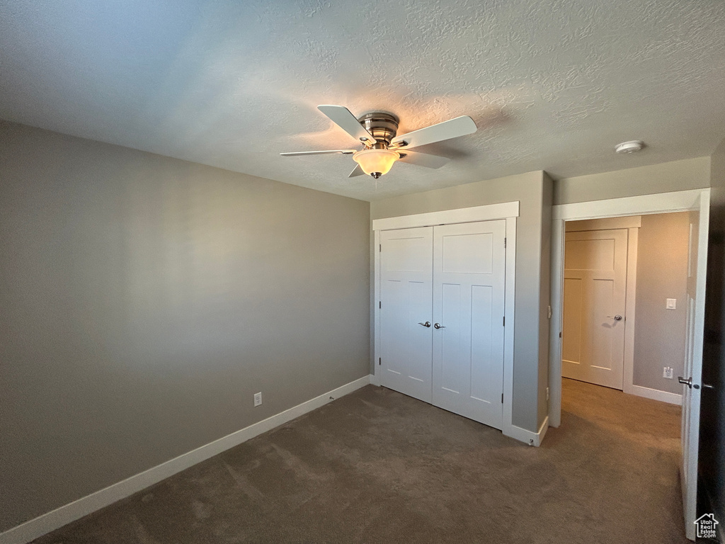 Unfurnished bedroom featuring baseboards, a ceiling fan, a closet, and dark colored carpet